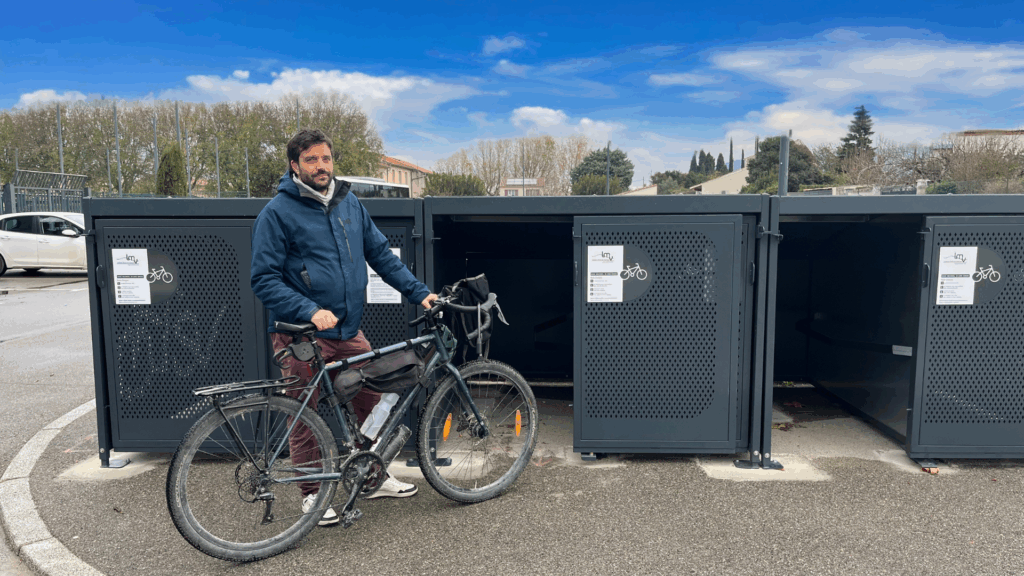 Un cycliste homme se tient pied à terre, son vélo en main devant un box vélo sécurisé - Agrandir l'image, fenêtre modale