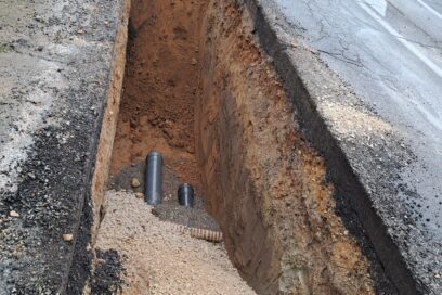 Photo illustrant la construction d'un réseau d'assainissement collectif public montrant un trou dans le sol profond avec la pose au fond du trou d'un gros tube d’assainissement - Agrandir l'image, fenêtre modale