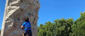 Enfant grimpant sur un mur d'escalade dans un parc, sous le regard d'un animateur qui l'assure, lors du Prox Raid Aventure qui s'est déroulé au parc du Grenouillet à Cavaillon en juillet 2022