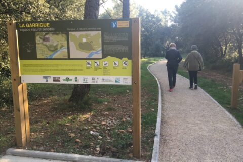 Départ du sentier de l'Espace Naturel La Garrigue de Mérdinol (accessible aux PMR). Deux femmes de dos marchent sur le sentier