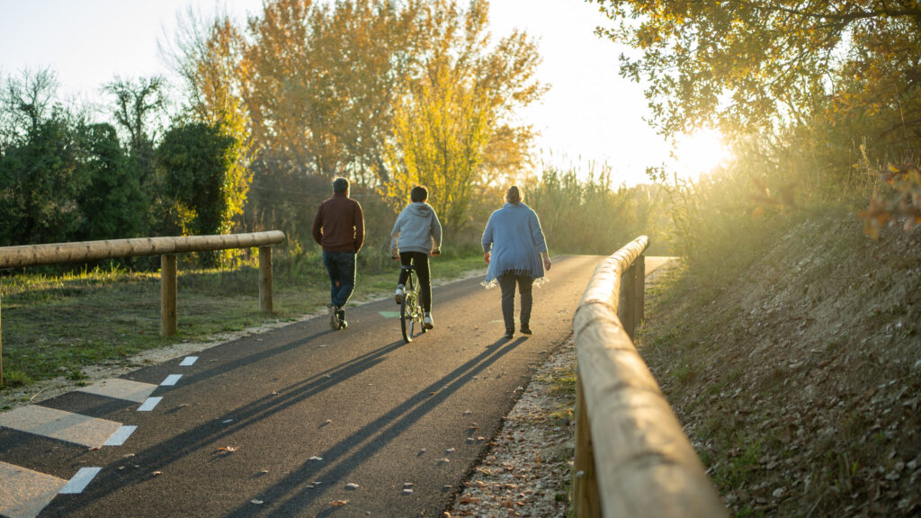 Famille de dos se baladant sur la véloroute du Calavon (parents à pied et fils à vélo) au coucher du soleil - Agrandir l'image, fenêtre modale