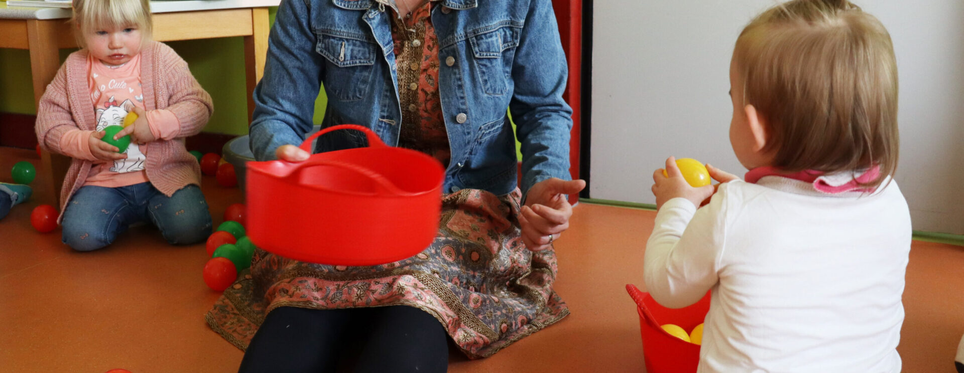 Animatrice de crèche assise au sol en train de faire un jeu de balle avec deux petites filles
