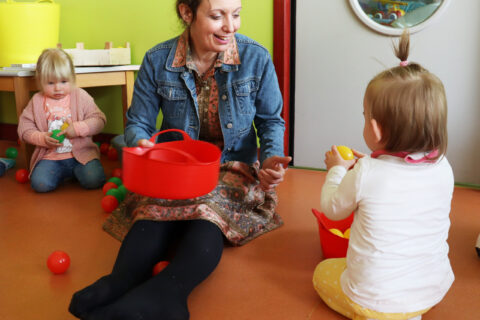 Animatrice de crèche assise au sol en train de faire un jeu de balle avec deux petites filles