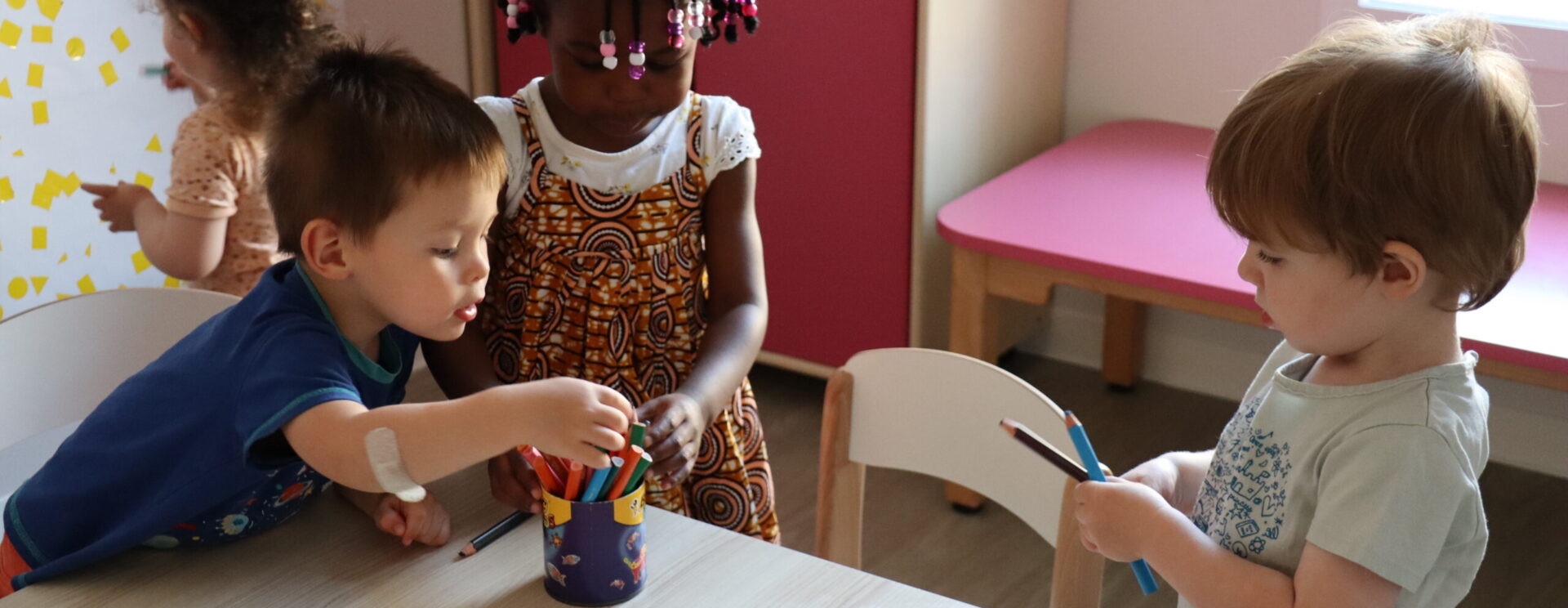 Trois jeunes enfants en crèche (deux garçons, une fille), en train de choisir des feutres
