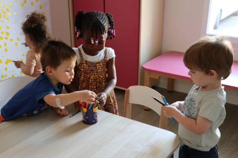 Trois jeunes enfants en crèche (deux garçons, une fille), en train de choisir des feutres