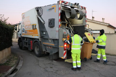 Deux agents de collecte LMV habillés en tenue de sécurité jaune fluo en train de vider un bac roulant de déchets dans un camion de collecte