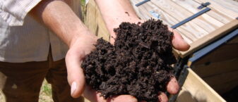 Gros plan de compost dans les mains d'un homme qui se tient devant un composteur