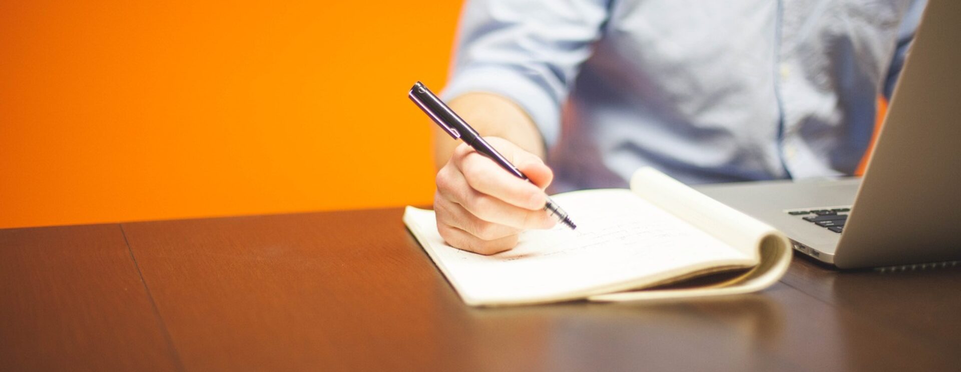 main tenant un crayon qui écrit sur un cahier près d'un écran d'ordinateur portable