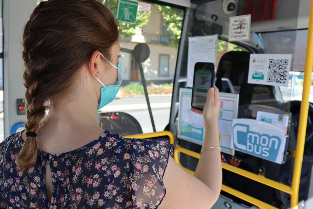 Jeune femme en train de valider son titre de bus dématérialisé directement dans un bus CmonBus, à l'aide de son smartphone - Agrandir l'image, fenêtre modale