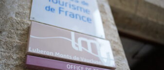 Gros plan de la plaque Office de tourisme accompagnée du logo LMV prise sur la porte de l'Office de tourisme de Gordes