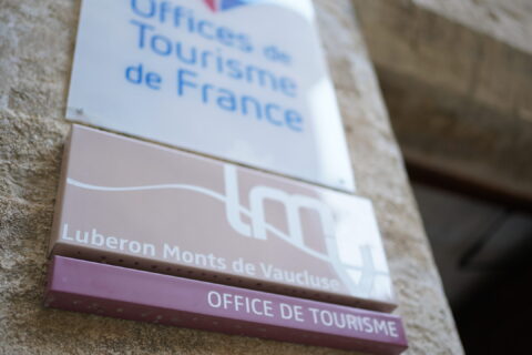Gros plan de la plaque Office de tourisme accompagnée du logo LMV prise sur la porte de l'Office de tourisme de Gordes