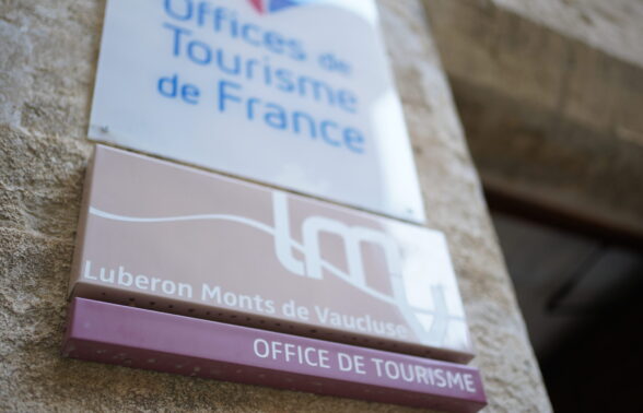 Gros plan de la plaque Office de tourisme accompagnée du logo LMV prise sur la porte de l'Office de tourisme de Gordes