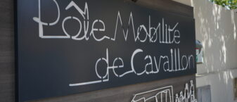 Gros plan de la plaque signalétique du Pôle Mobilité de Cavaillon, écrite en fil de fer tordu et avec dessous un bus et une famille dessinée de la même façon