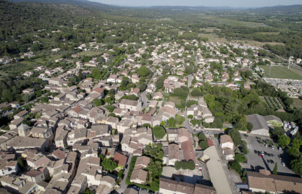 Mérindol vue d'un drone. Au premier plan : le village, l'école, la médiathèque. A droite : le stade. au fond : l'Espace Naturel Sensible La Garrigue