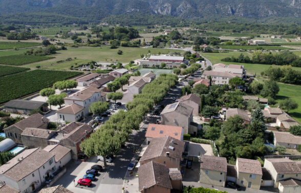 Oppède vue d'un drone. Au premier plan : la rue des Poulivets qui dessert la mairie, l'école, la médiathèque. Au 2e plan : la plaine. Au fond : Le Luberon