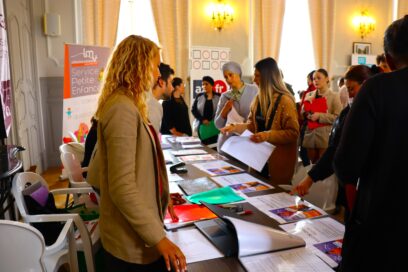 Stand sur lequel des personnes se renseignent et regardent des documents posés sur une table qui sépare les recruteurs des chercheurs d'emploi - Agrandir l'image, fenêtre modale