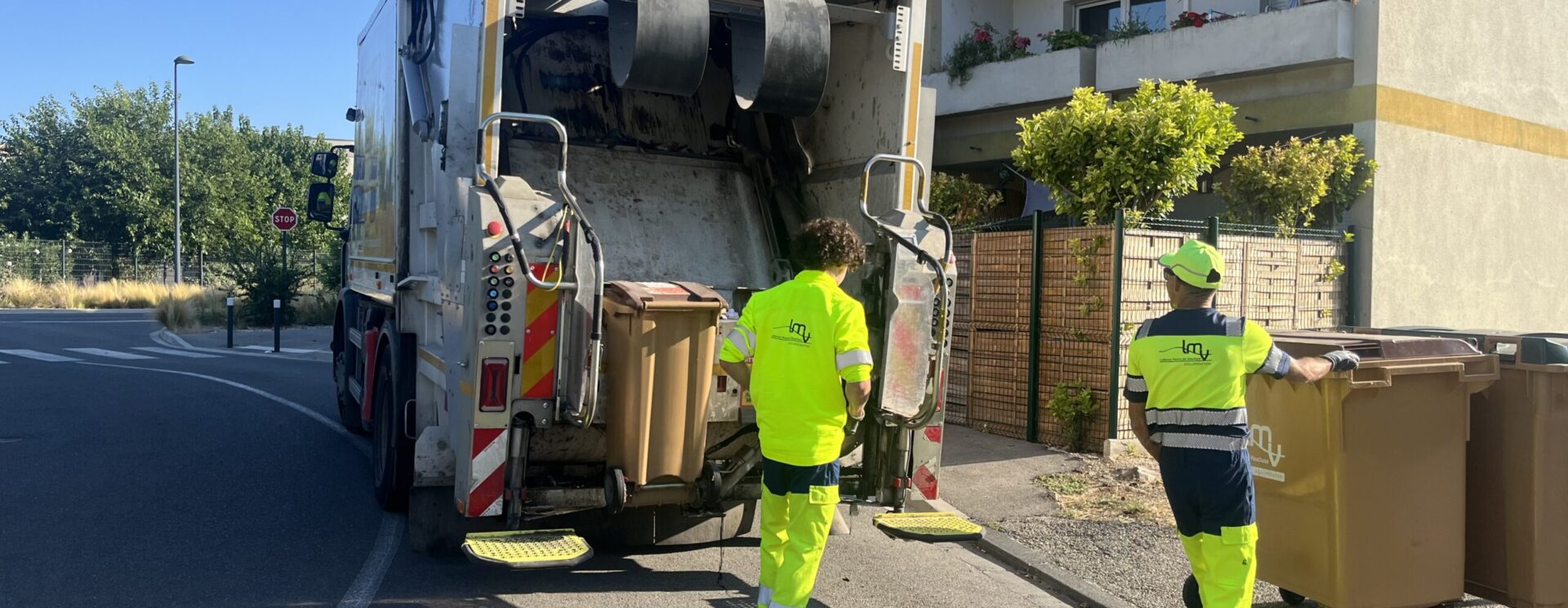 Agents de collecte en train de vider une poubelle devant un camion de collecte