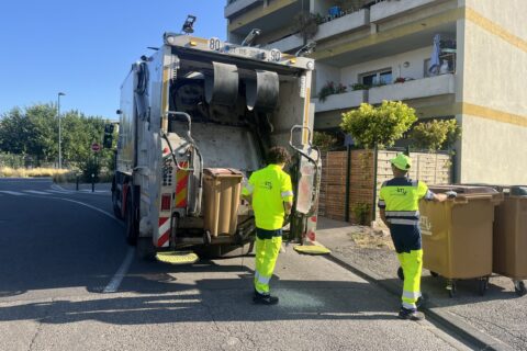 Agents de collecte en train de vider une poubelle devant un camion de collecte